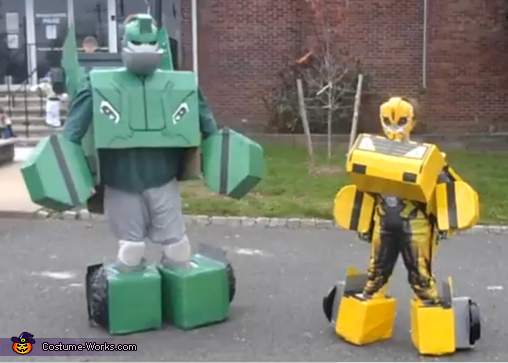 Two power rangers in larger boxy costumes, boxes around their feet and hands protrude out.